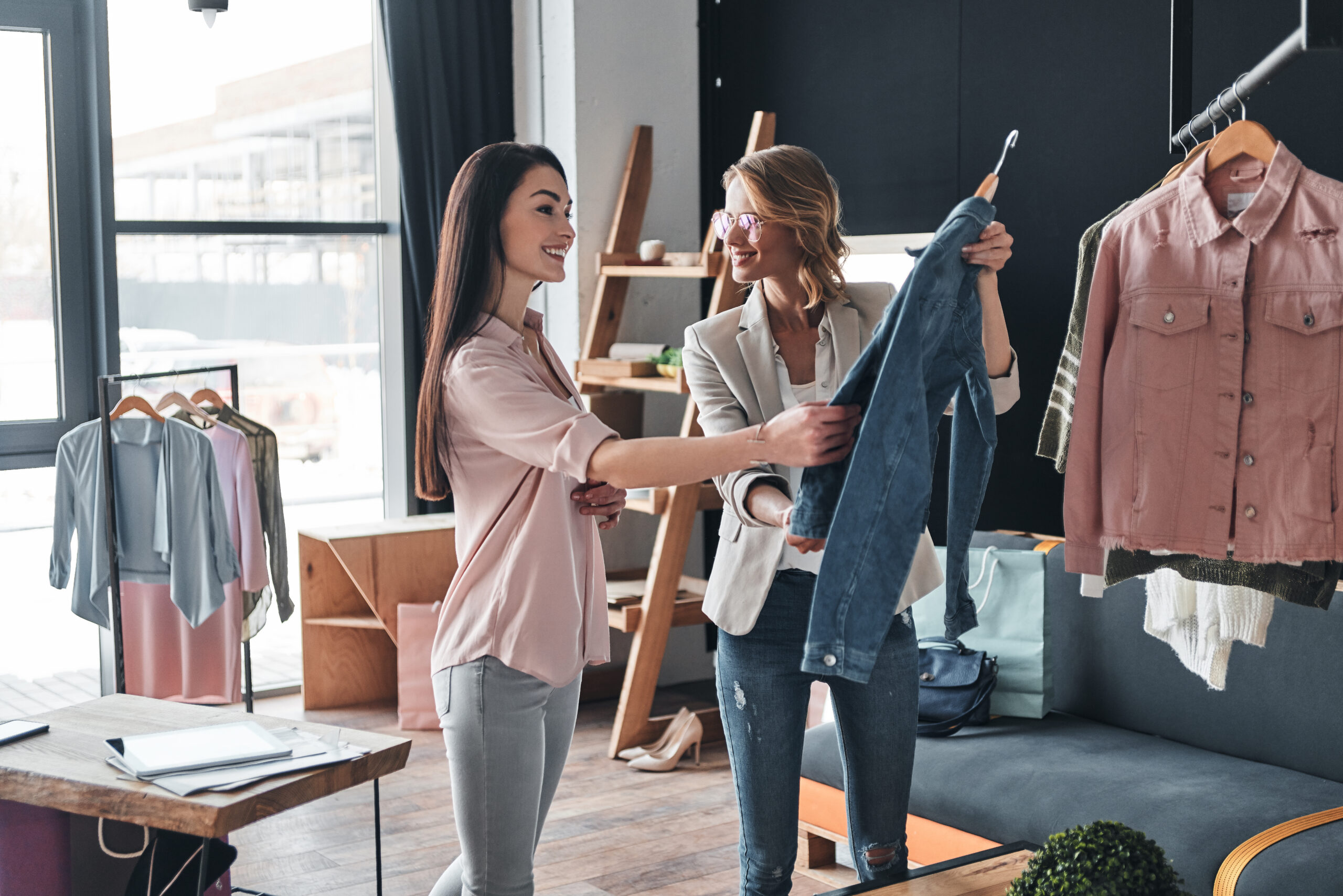 Beautiful Young Woman Helping to Choose Clothes to Her Customer While Working in the Fashion Boutique